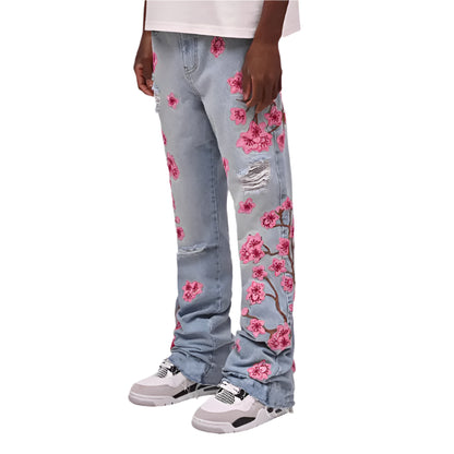 Light blue jeans with pink floral patterns worn by a person on a white background